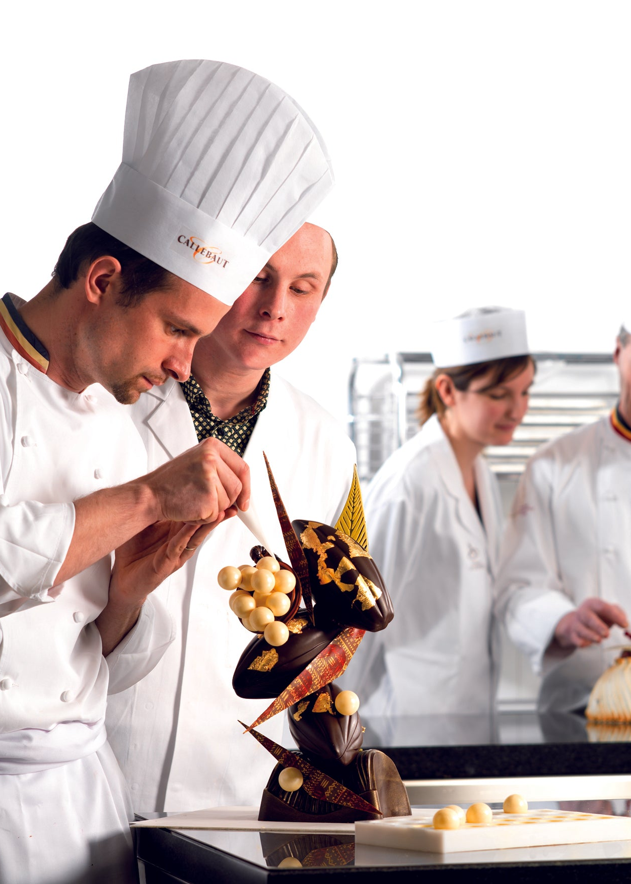 Professionelle Konditoren in einer Gastronomieküche arbeiten an kunstvollen Schokoladenskulpturen und Desserts mit Callebaut Kuvertüre und Backschokolade. Ideal für Schokolade für Profis, Gastronomiebedarf, Bäckereibedarf, Konditoreibedarf, Cafébedarf und Restaurantbedarf.