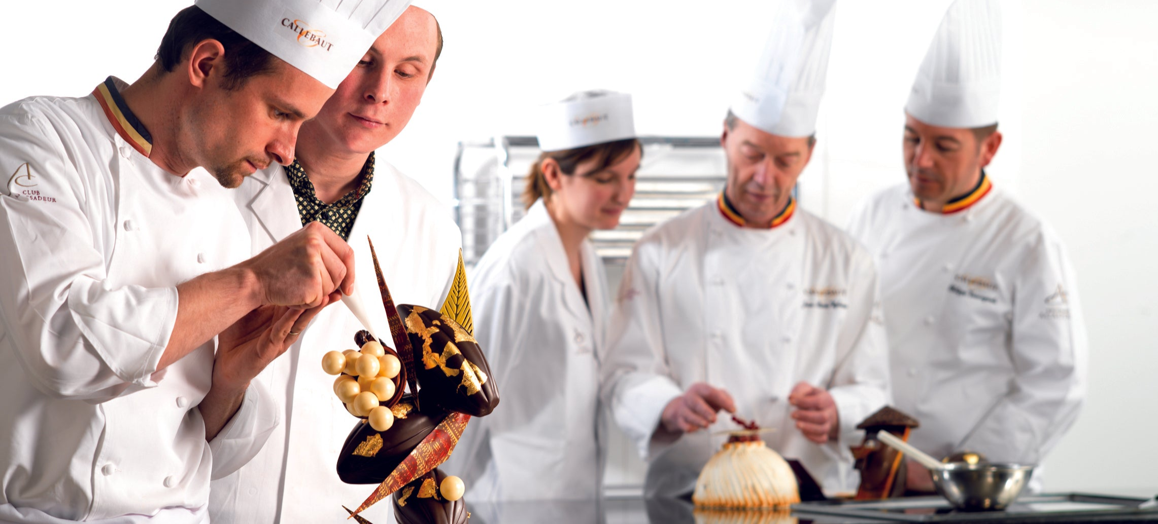 Professionelle Konditoren in einer Gastronomieküche arbeiten an kunstvollen Schokoladenskulpturen und Desserts mit Callebaut Kuvertüre und Backschokolade. Ideal für Schokolade für Profis, Gastronomiebedarf, Bäckereibedarf, Konditoreibedarf, Cafébedarf und Restaurantbedarf. 